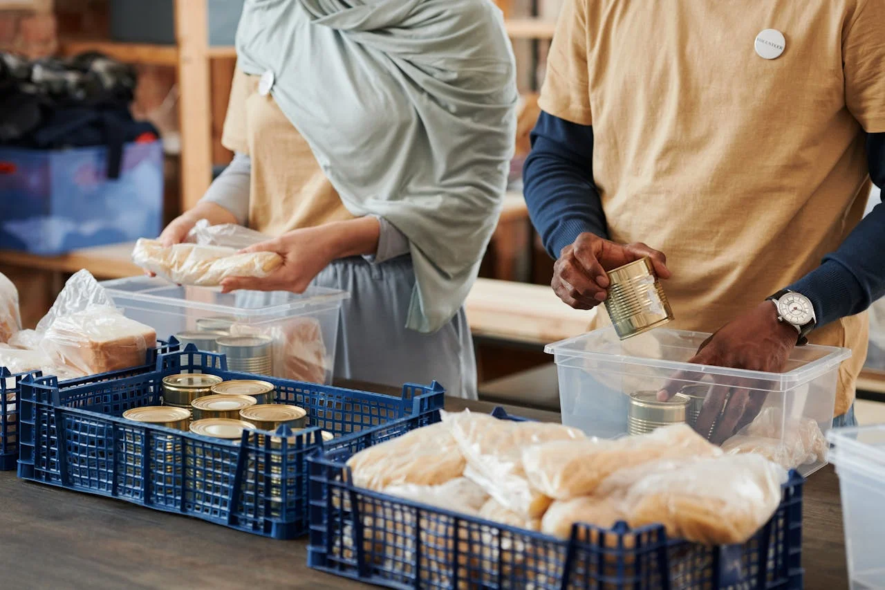 Adults sorting food donations in containers for charity. Community service effort indoors.